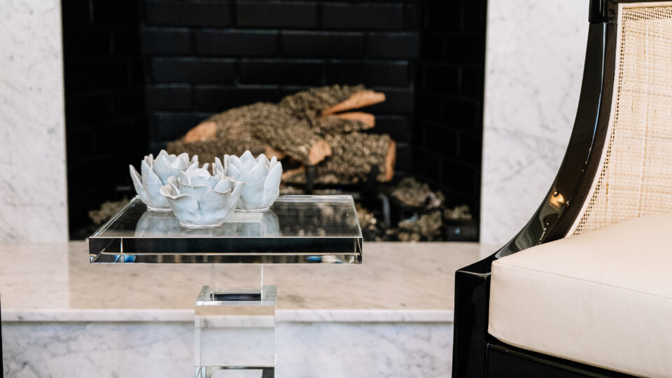 Detail of marble fireplace with acrylic side table and ceramic flowers in a Franklin Lakes NJ luxury living room design.