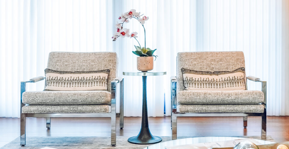 Pair of modern upholstered chairs with chrome frames flanking a round pedestal side table topped with an orchid centerpiece.